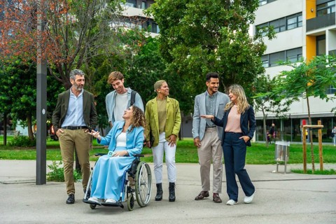 Diverse group of business people, including a woman in a wheelchair, engaging in a lively outdoor
