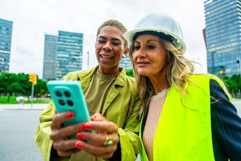 Diverse women architects and engineers smiling and collaborating outdoors in a modern city, using a