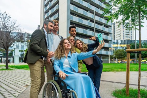 Diverse group of business colleagues, including a woman in a wheelchair, smiling and taking a