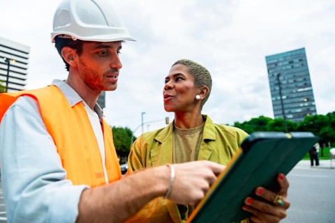Construction engineer wearing a hard hat and safety vest pointing to a digital tablet while having