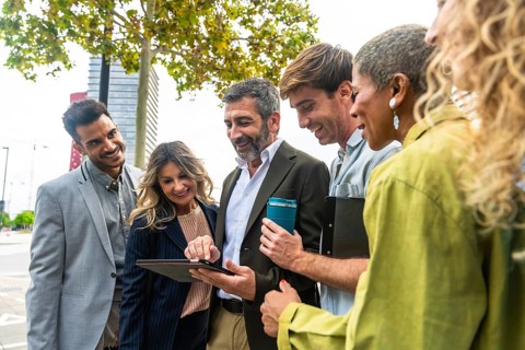 Diverse group of smiling business people looking at a tablet screen together, discussing ideas and