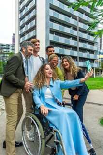 Diverse group of smiling colleagues with a woman in a wheelchair taking a cheerful selfie together