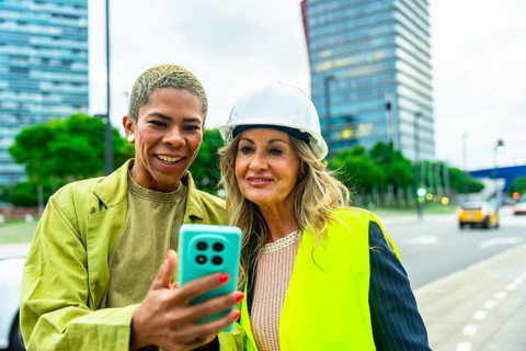 Diverse women architects and engineers smiling outdoors, looking at a smartphone screen,