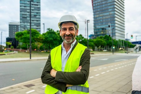 Senior construction professional in hard hat and high visibility vest stands with arms crossed,