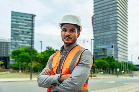 Professional engineer or architect standing confidently with crossed arms, wearing a hardhat and