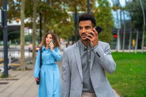 Business colleagues walking on a city sidewalk while communicating on their mobile phones, focusing