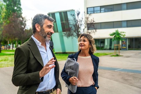 Two business colleagues, a man and a woman, walking together in an urban park setting while