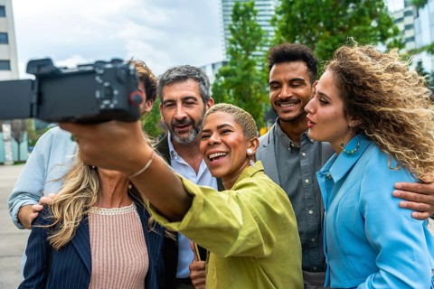 Diverse group of smiling business professionals vlogging outdoors, capturing content together for