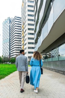 Two business professionals walking together along a paved pathway in an urban area, passing tall