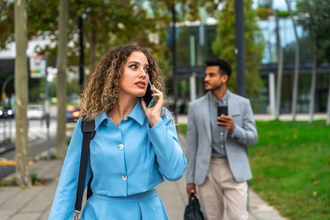 Confident businesswoman talking on her smartphone while walking on a city sidewalk with a male