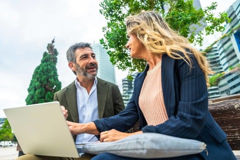 Two business colleagues engaged in a discussion while working on a laptop, sitting together on a