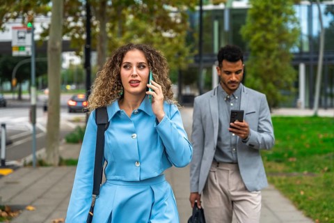 Businesswoman talking on her mobile phone while walking on a city sidewalk with a male colleague