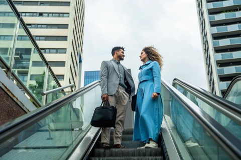 Two business professionals ascending an escalator, engaging in a conversation with modern