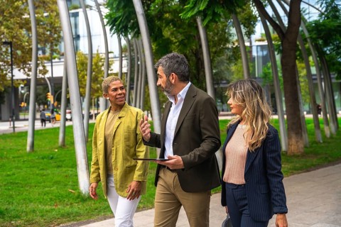 Three diverse business colleagues walking together in an urban park, engaging in a lively outdoor