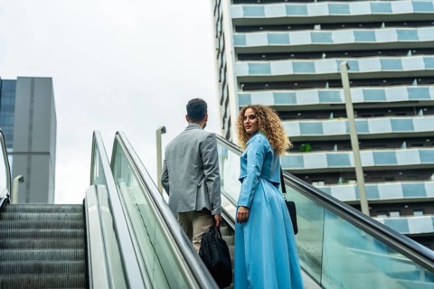 Two diverse business colleagues ascending an escalator, looking towards a modern city building,