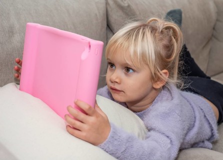 Portrait of a blonde girl, 4 years old, lying down reading a tablet in Ystad, Skåne County, Sweden,