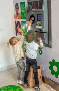Two children, 5 and 7 years old, earn pocket money by recycling cans in a recycling machine in