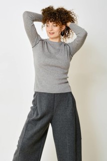 A woman stands with her hands behind her head, showcasing a cozy grey long-sleeve top paired with