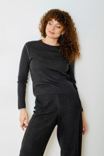 Relaxed woman stands in a cozy dark grey outfit that includes a stylish top and matching pants. The