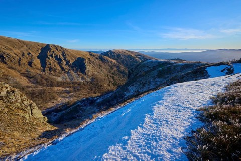Snowy mountain slopes under blue sky revealing a vast valley and mountains, winter, Route de