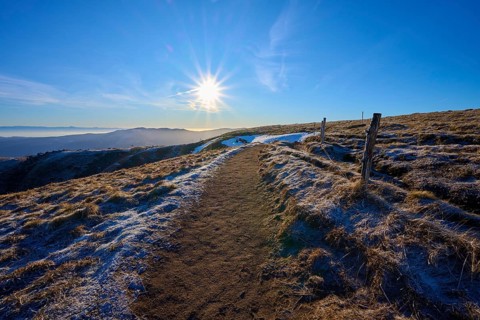 Path on a frosty mountain ridge in sunlight, with a wide view of peaceful nature, winter, Route de