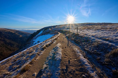 A sunny trail leads over a frosty mountain surrounded by clear air and blue skies, winter, Route de