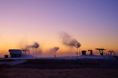 Snow cannons blow smoke under purple and orange evening sky, winter, Route de Cretes, Hohneck, La