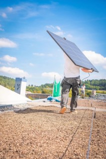 A worker carries a solar panel over the roof in sunny weather and blue skies, new park and ride