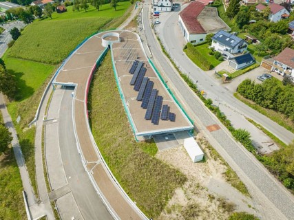 Large solar panel system on roof surrounded by rural village and greenery, new park and ride
