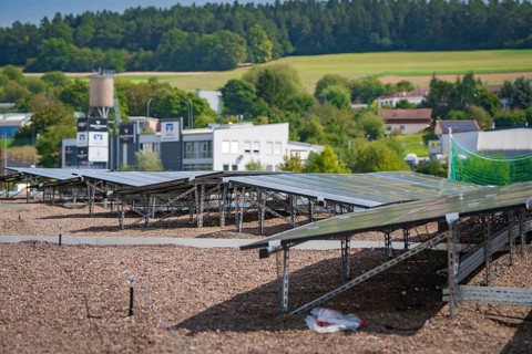 Solar panels on a roof with a view of a green landscape and nearby buildings, new park and ride