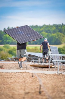 Workers install solar panels with cables in an open field under a blue sky, new park and ride