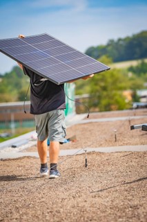 Man carrying solar panel on a gravel roof in front of a natural landscape, new park and ride