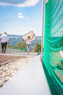 Worker carrying a solar panel on a construction site with a view of the mountains, new Park and