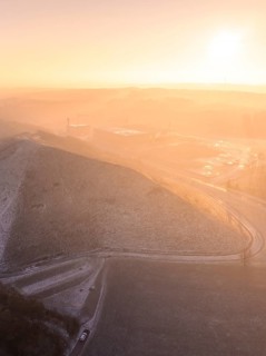 Snow-covered hilltop in soft orange light of morning sun, old deposit, construction site for PV