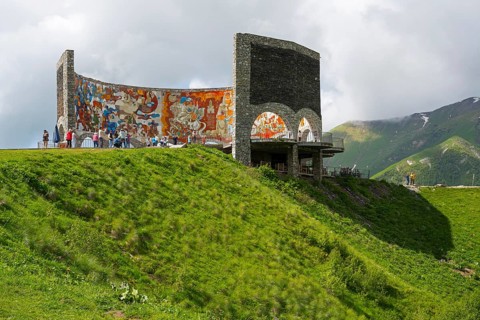 Grassy hill with painted wall, people enjoying the view, Georgian-Russian Friendship Memorial,