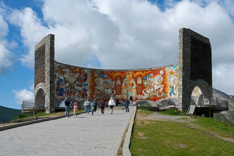 People look at a large wall painting on a curved stone wall, Georgian-Russian Friendship Memorial,