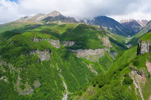 Green mountains with deep gorges under cloudy sky, mountainous landscape between Gudauri and Cross
