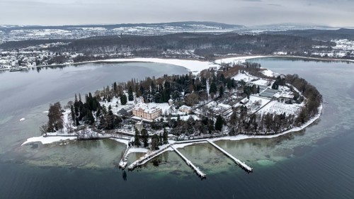 The wintry and snowy Mainau island in Lake Constance with the pier and the baroque Mainau Castle,