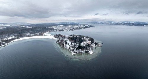 The wintry and snowy Mainau island in Lake Constance with the pier and the baroque Mainau Castle,
