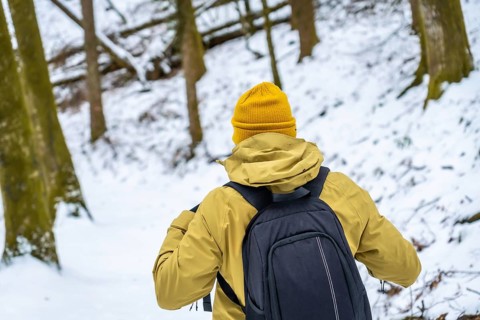 Hiker with backpack and yellow beanie navigating a snow covered forest, embracing the cold weather