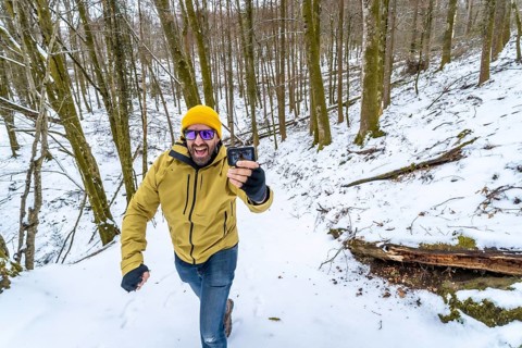 Happy man in a yellow beanie and green jacket smiling at his action camera while vlogging on a