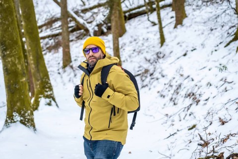 Adult male adventurer, wearing a yellow beanie, yellow jacket, sunglasses, and backpack, walking