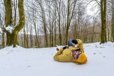 Man wearing a yellow winter jacket and hat, sunglasses, lying relaxed on the snow covered ground in