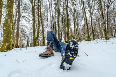 Person lying down in deep snow wearing warm hiking boots with a visible non slip sole, experiencing