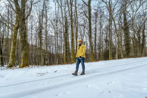Man in a yellow jacket, beanie, and sunglasses exploring a snow covered forest path, enjoying the