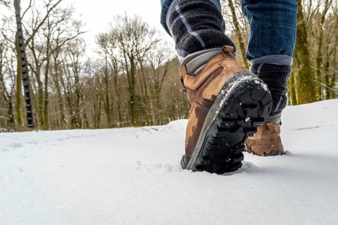 Person walking through a winter forest landscape wearing brown hiking boots, their soles visible