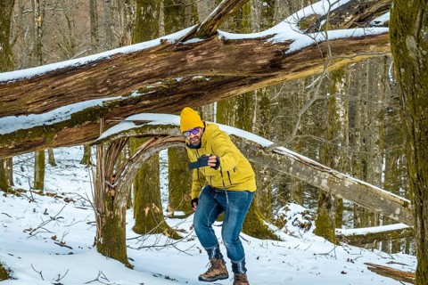 Man documenting outdoor adventure in a snow covered forest, holding a camera and filming himself