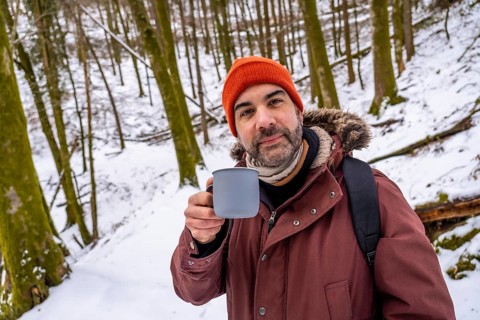 Man with an orange beanie and a winter coat holding a mug of a hot beverage, finding warmth and