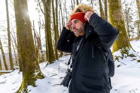 Man photographer adjusting his jacket or coat hood with fur trim while wearing a beanie and scarf