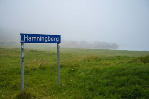 Town sign for Hamningberg on the Barents Sea in the midst of grassy landscape with fog and calm